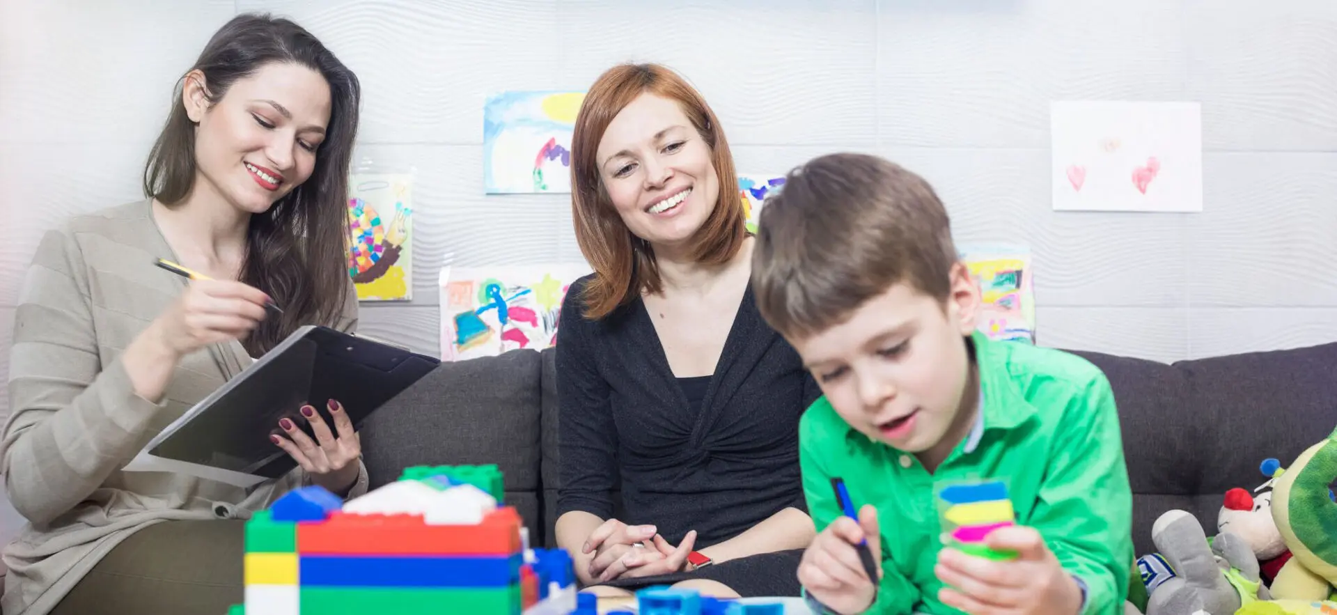 A woman joyfully watches a boy playing with colorful building blocks.