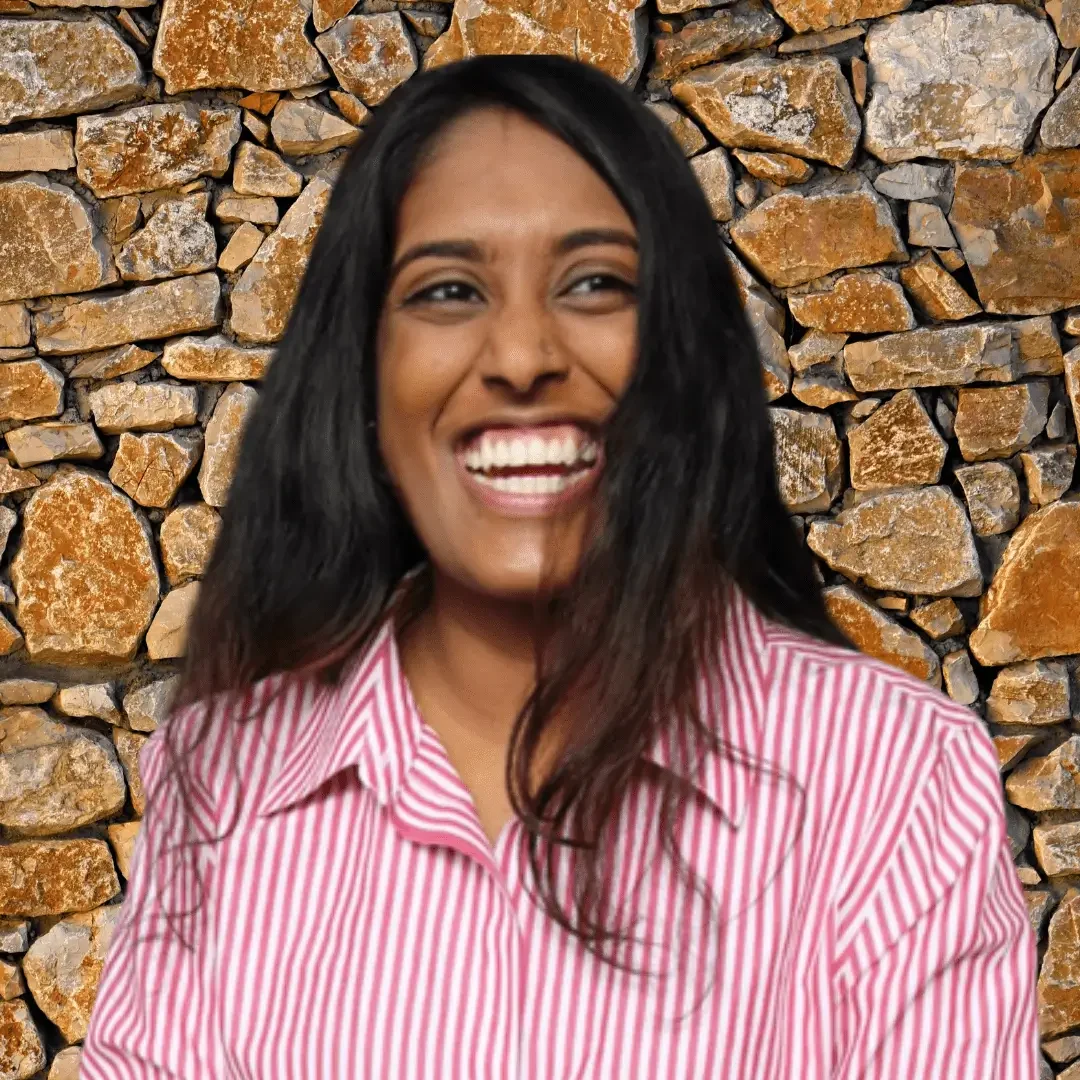 A woman with long black hair smiles against a stone wall backdrop.