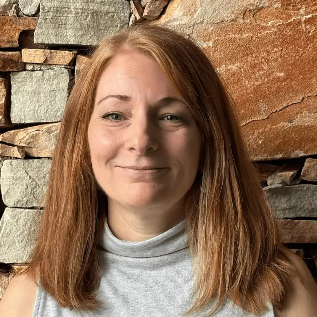 Woman with red hair smiling against a stone wall background.