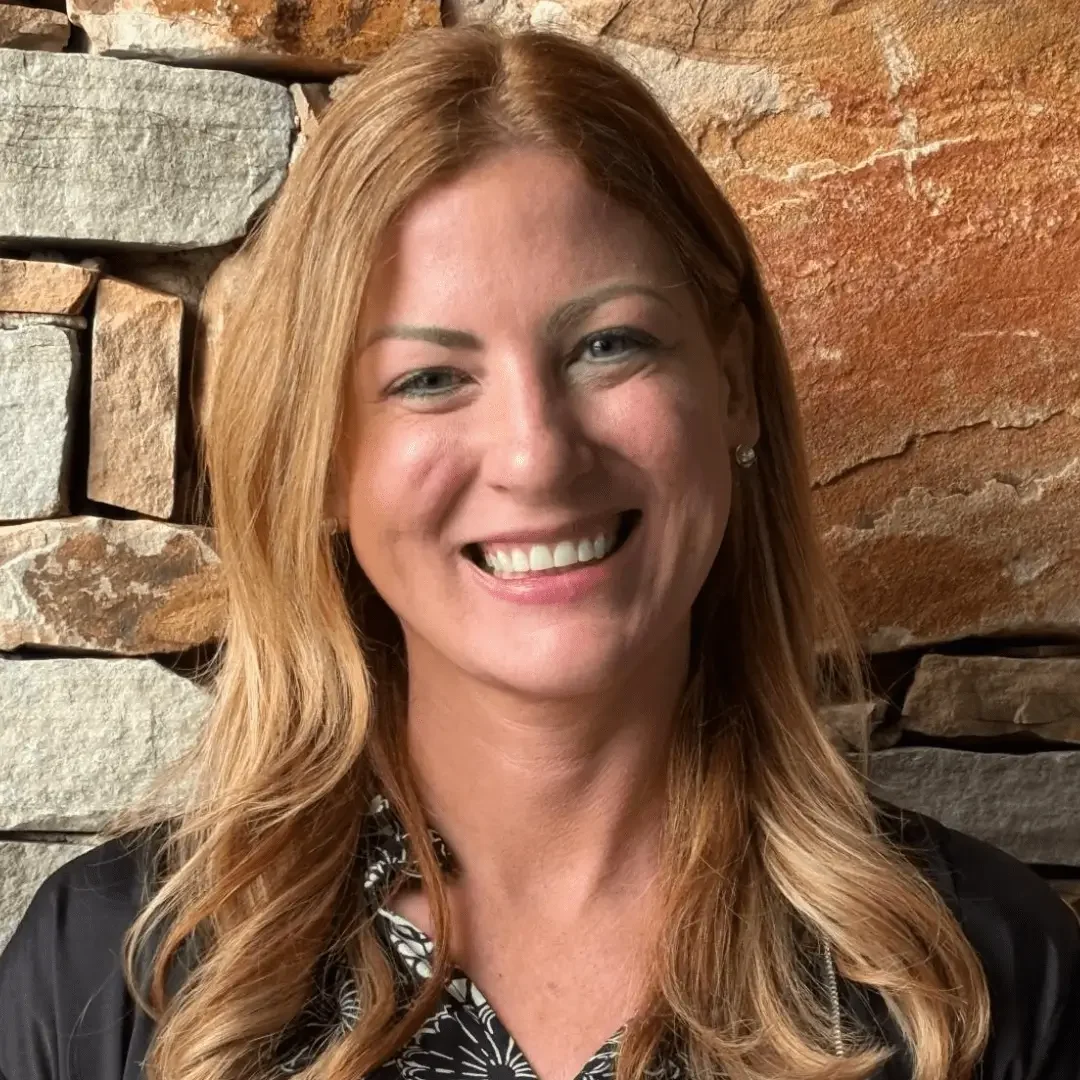 Smiling woman with long blonde hair in front of a stone wall.